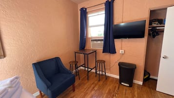 Een kamer met een blauwe stoel, een kleine tafel met krukken, een aan de muur bevestigde televisie en een prullenbak.