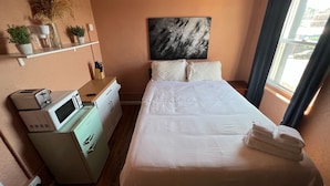 Ein Hotelzimmer mit Bett, Mikrowelle, einer kleinen Küchenzeile, einem Bild an der Wand und einem Fenster mit Vorhängen.