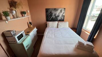 Hotelkamer met een bed, magnetron, een klein kitchenette, een schilderij aan de muur en een raam met gordijnen.