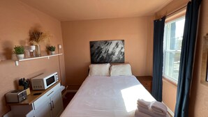 Ein Hotelzimmer mit einem Bett, einer Mikrowelle, einer kleinen Küchenzeile, einem Fenster mit Vorhängen und einem an der Wand hängenden Kunstwerk.