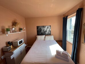 Ein Hotelzimmer mit einem Bett, einer Mikrowelle, einer kleinen Küchenzeile, einem Fenster mit Vorhängen und einem an der Wand hängenden Kunstwerk.