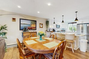 A modern kitchen with white cabinets, a stainless steel refrigerator, and a dining area with a wooden table and chairs. - Lakeside Escape:  views and walk to beach (Center Ossipee)