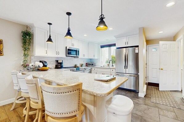 Een moderne keuken met witte kasten, een centraal eiland, hanglampen en roestvrijstalen apparatuur.