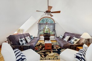 A cozy living room with a high ceiling, a ceiling fan, a large window with checkered curtains, and a television. - 1 BR plus downtown - walk to Beaches/ Eateries (Kennebunkport)