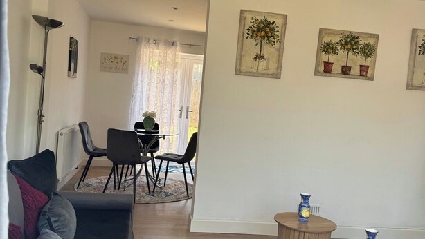 Uma sala de estar com sofá, área de refeições com cadeiras, uma mesinha e um lustre.