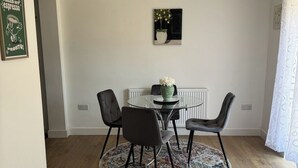 Uma sala de jantar com uma mesa redonda, quatro cadeiras, um vaso com flores, um quadro na parede e um radiador.