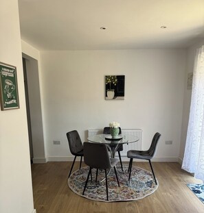 Ein Essbereich mit einem runden Tisch, vier Stühlen, einer Blumenvase, einem Bild an der Wand und einer Heizung.
