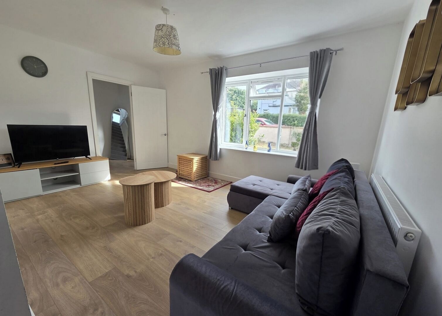 A modern living room with a sofa, TV, wooden coffee table, and a view of the outside.