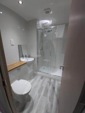 A modern bathroom with a toilet, sink, and glass-enclosed shower. - The Queensberry (Dumfries)