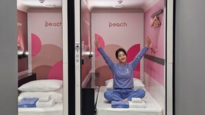 A room with a bed, a wall-mounted towel dispenser, and a wall with the word 'peach' visible. - FIRST CABIN SEOUL MYEONGDONG (Seoul)