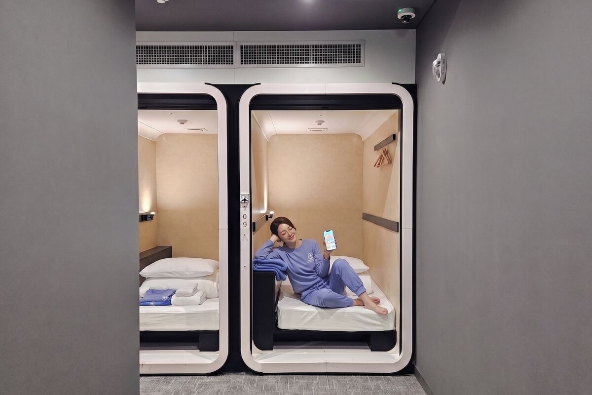 A hotel room with two beds, a person sitting on one bed, and a smartphone in hand.