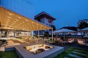 A hotel exterior with a covered outdoor seating area, a first cabin sign, and a modern building in the background. - FIRST CABIN SEOUL MYEONGDONG (Seoul)