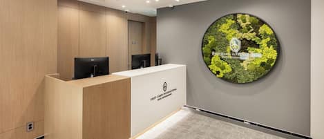 A reception area with a wooden reception desk, a circular wall decoration, and a grey carpeted floor.
