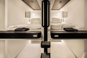 A mirrored room with two beds, a central pole, and a fold-down desk with a suitcase. - FIRST CABIN SEOUL MYEONGDONG (Seoul)