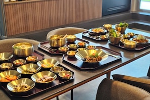A dining table with multiple metal bowls containing various dishes, arranged on a wooden table in a room with a modern design. - FIRST CABIN SEOUL MYEONGDONG (Seoul)
