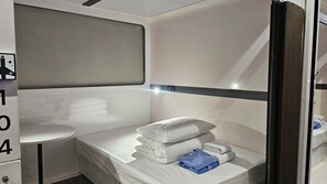 A compact hotel room with a bunk bed, a small round table, and a wall-mounted shelf. - FIRST CABIN SEOUL MYEONGDONG (Seoul)