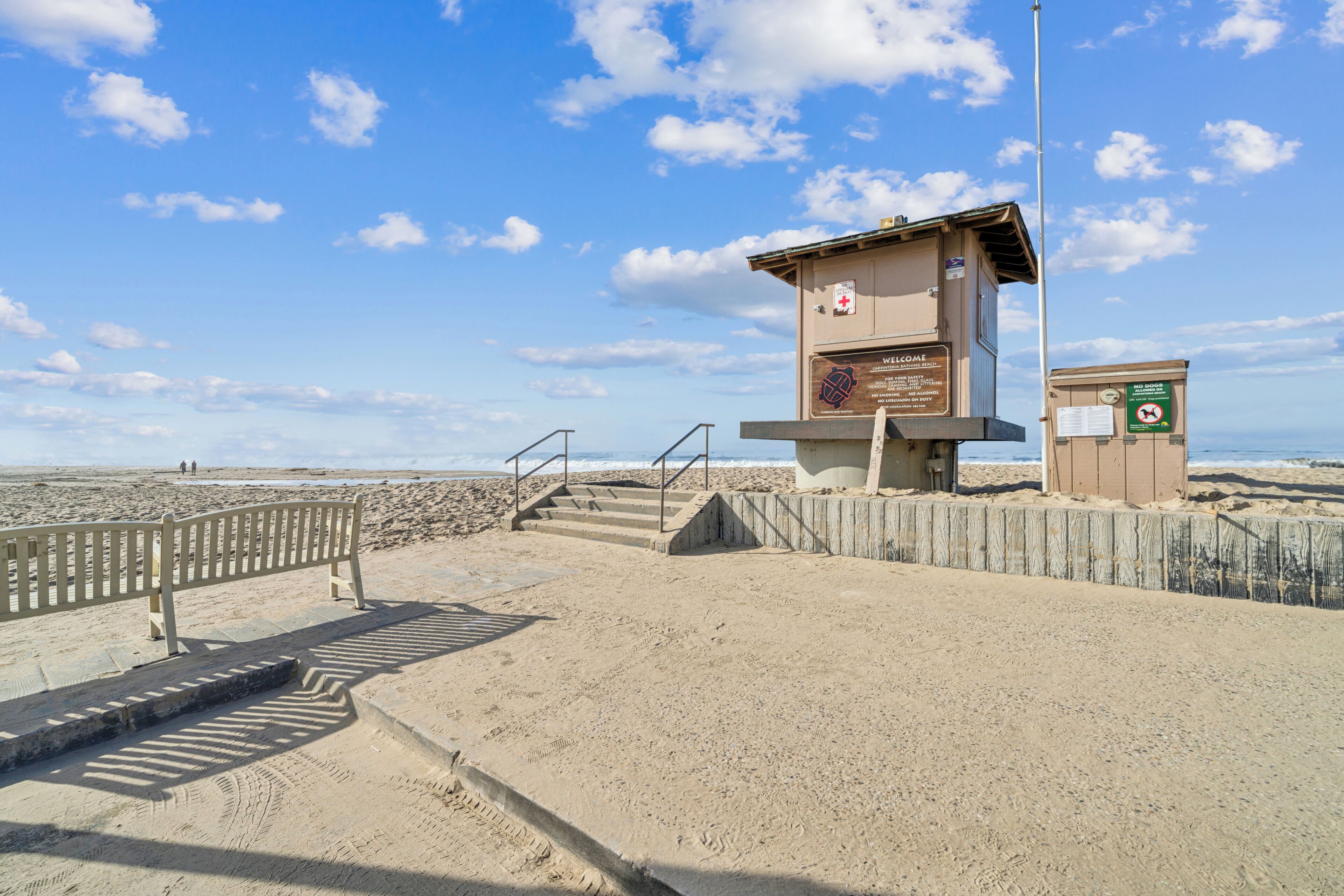 Ein Rettungsschwimmturm mit einem Schild, einer Holzbank und einem Sandstrand.