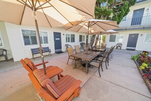 En patio med et træbord og stole, en stor parasol samt en række døre nummereret 121 til 124.