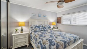 Une chambre à coucher comprenant un lit, deux tables de chevet, un ventilateur de plafond et des éléments de décoration murale.