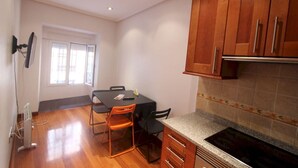 A compact kitchen with wooden cabinets, a dining table with chairs, and a built-in stove. - Apartamentos Good Stay Atocha (Madrid)