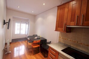 A compact kitchen with wooden cabinets, a dining table with chairs, and a built-in stove. - Apartamentos Good Stay Atocha (Madrid)