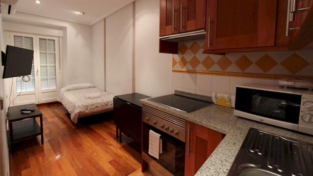 A compact kitchen with wooden cabinets, a stove, microwave, and a small dining area with a table and chairs. - Apartamentos Good Stay Atocha (Madrid)