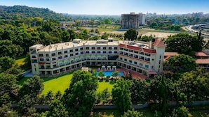 A multi-story hotel with a courtyard, surrounded by greenery and a view of a cityscape. - Vits Kamats Resort (Silvassa)