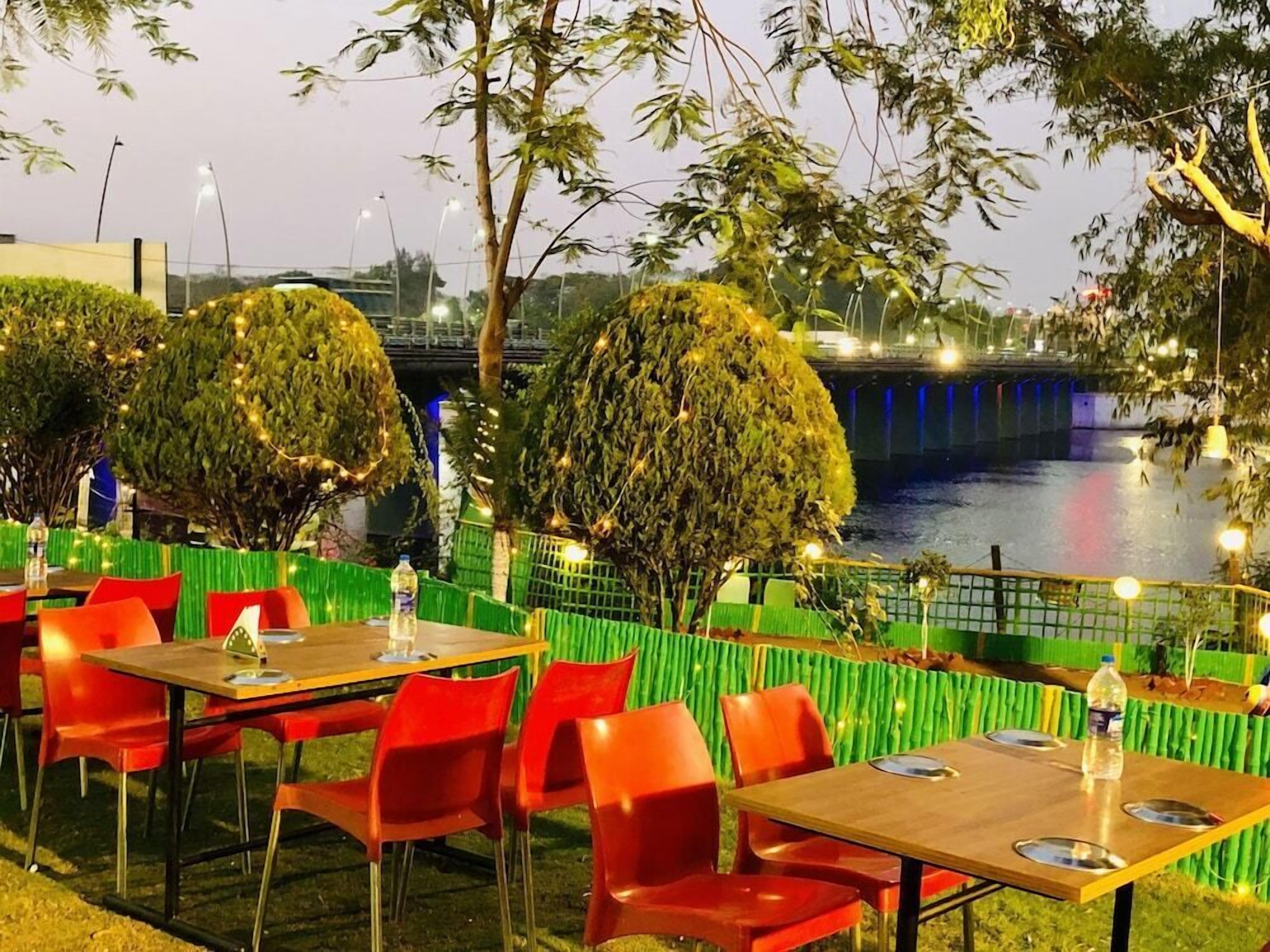 An outdoor dining area with tables and chairs, a river in the background, and a bridge.