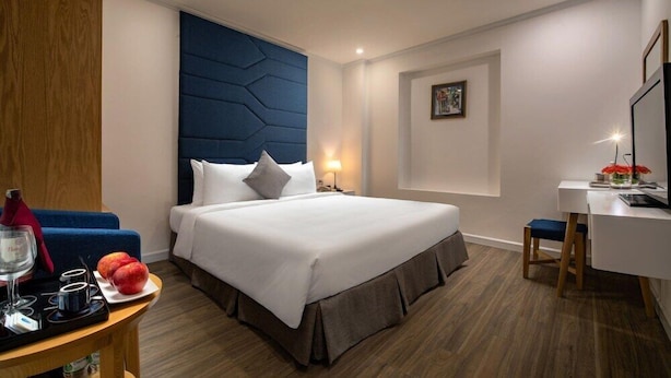 A hotel room with a bed, bedside table, desk, chair, and a wall-mounted TV. - Bonsella Cozy Hotel (Hanoi)