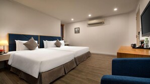 A hotel room with a double bed, bedside tables, a desk, a chair, an air conditioning unit, and a television. - Bonsella Cozy Hotel (Hanoi)
