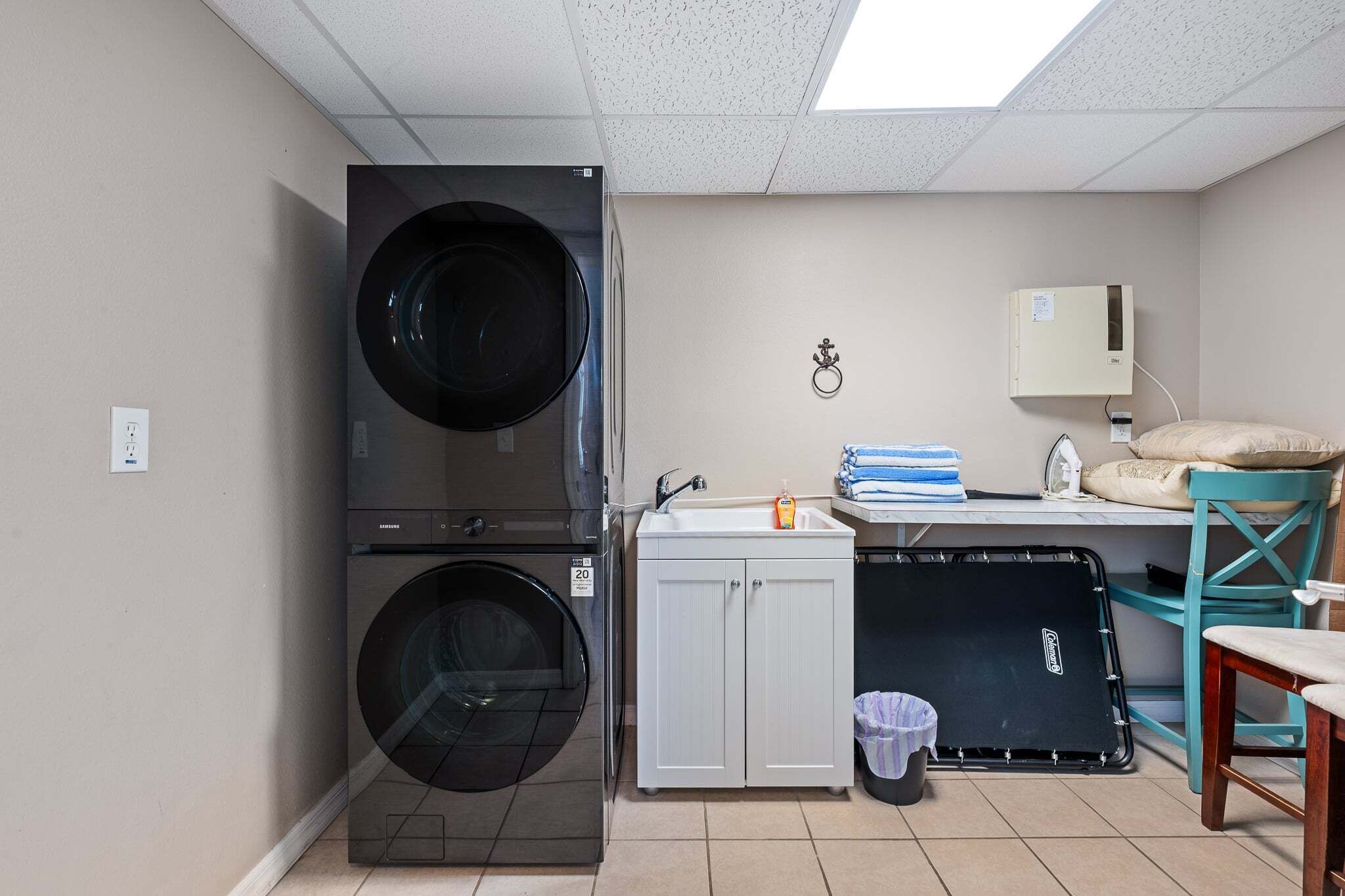 Une buanderie équipée d’un lave-linge et d’un sèche-linge superposés, d’un évier, de placards et d’une chaise.