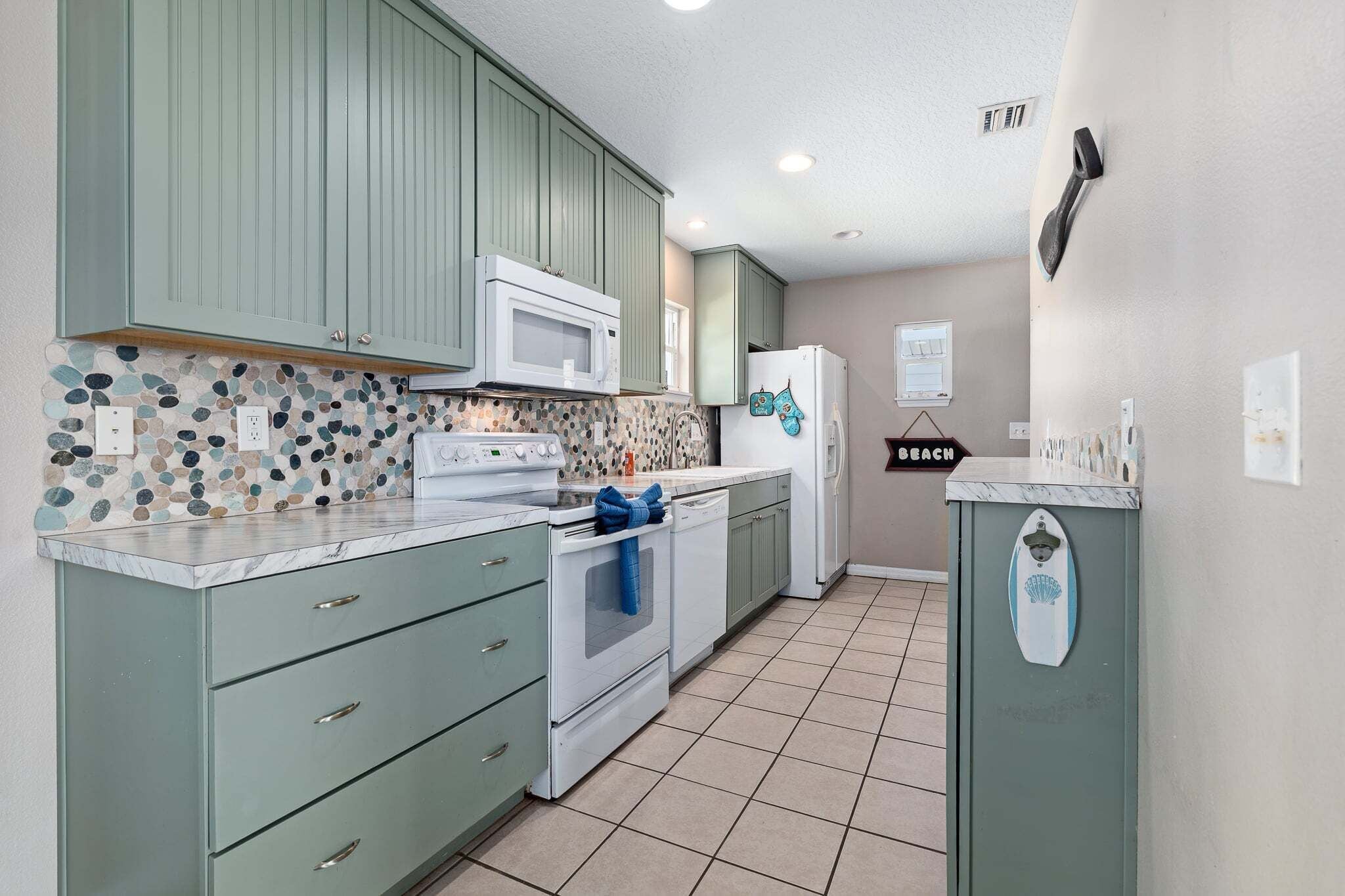 A kitchen with green cabinets, a white microwave, a white refrigerator, and a tiled backsplash.