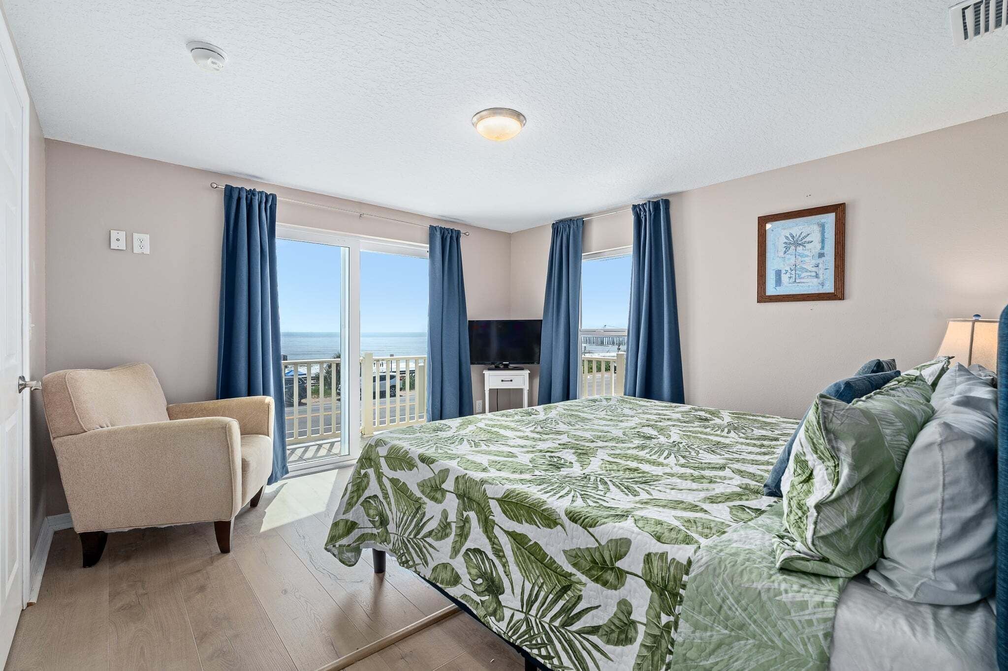 A hotel room with a bed, a chair, a TV, and a balcony with a view.