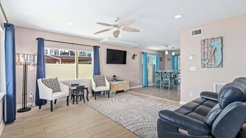 Ein modernes Wohnzimmer mit einer Couch, Sesseln, einem Esstisch und einem Deckenventilator.