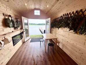 A cabin with a wooden interior, a table, chairs, a fireplace, and a view of a lake. - Cabin - House of the Muse (Gordon)