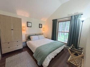A bedroom with a bed, bedside lamps, a window with curtains, a wardrobe, and a wooden chair. - Cabin - House of the Muse (Gordon)