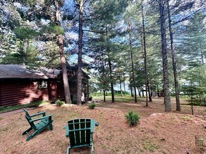 A cabin surrounded by tall trees, with a picnic table and chairs in the foreground. - Cabin - House of the Muse (Gordon)