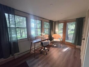 Habitació amb escriptori, cadira i finestres grans que donen vista a l'exterior.