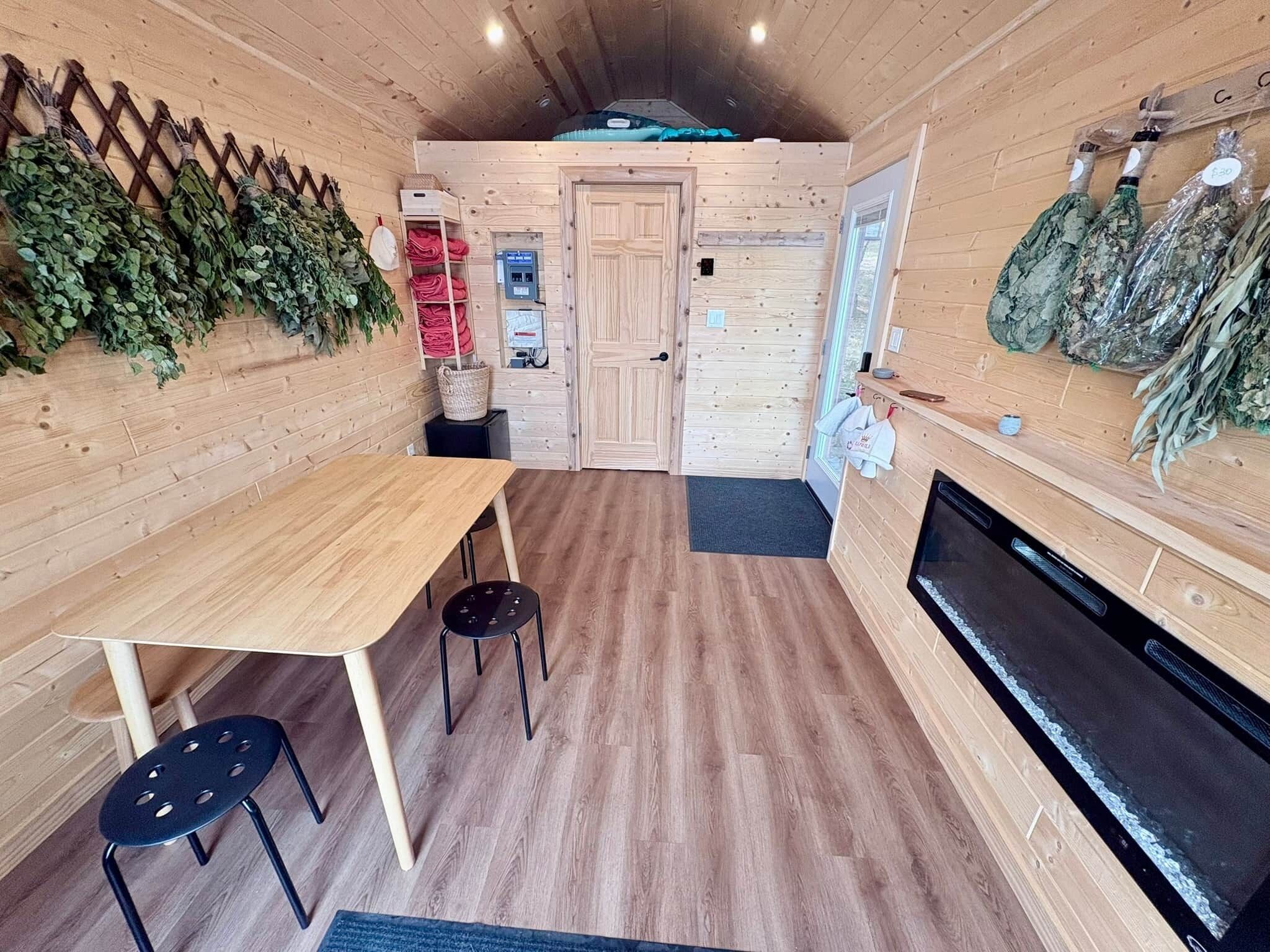 A wooden interior with a dining table, chairs, a fireplace, and a wall-mounted herb rack.