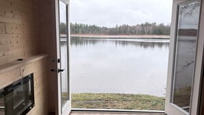 Ein Zimmer mit einer großen Schiebeglaswand, die zu einem See führt, einem Kamin und Holzwänden.