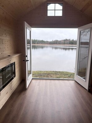Ein Zimmer mit einer großen Schiebeglaswand, die zu einem See führt, einem Kamin und Holzwänden.