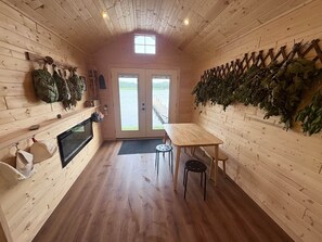 A wooden cabin interior with a dining table, chairs, a fireplace, and a view of a dock through the door. - Cabin - House of the Muse (Gordon)