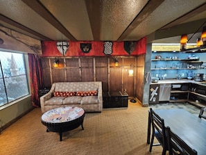 A cozy room with a sofa, a round coffee table, a fireplace, and a kitchen area with shelves. - Wizard-Themed Condo Near Universal (Orlando)