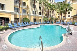 A swimming pool surrounded by lounge chairs and palm trees. - Wizard-Themed Condo Near Universal (Orlando)