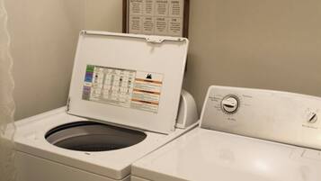 A laundry area with a front-loading washer and dryer, a shelf with folded towels, and a laundry guide on the wall.