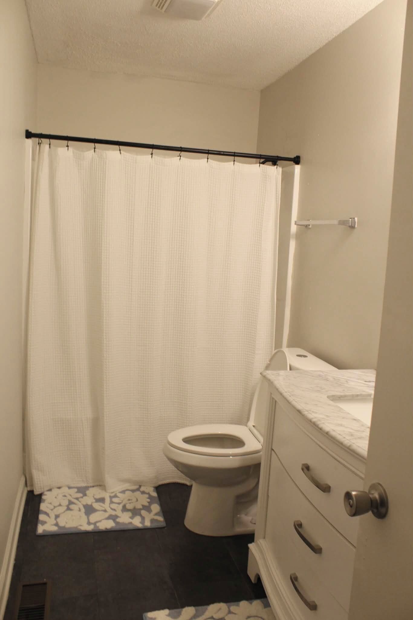 A bathroom with a toilet, a shower curtain, a sink, and a patterned mat.