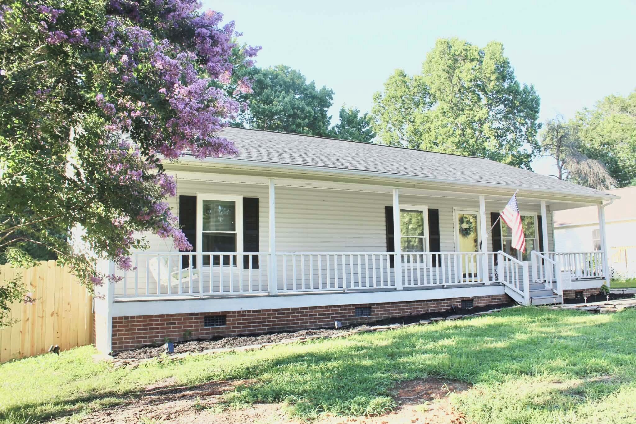 A single-story house with a front porch, a brick foundation, and a flag.