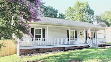 A single-story house with a front porch, a brick foundation, and a flag.