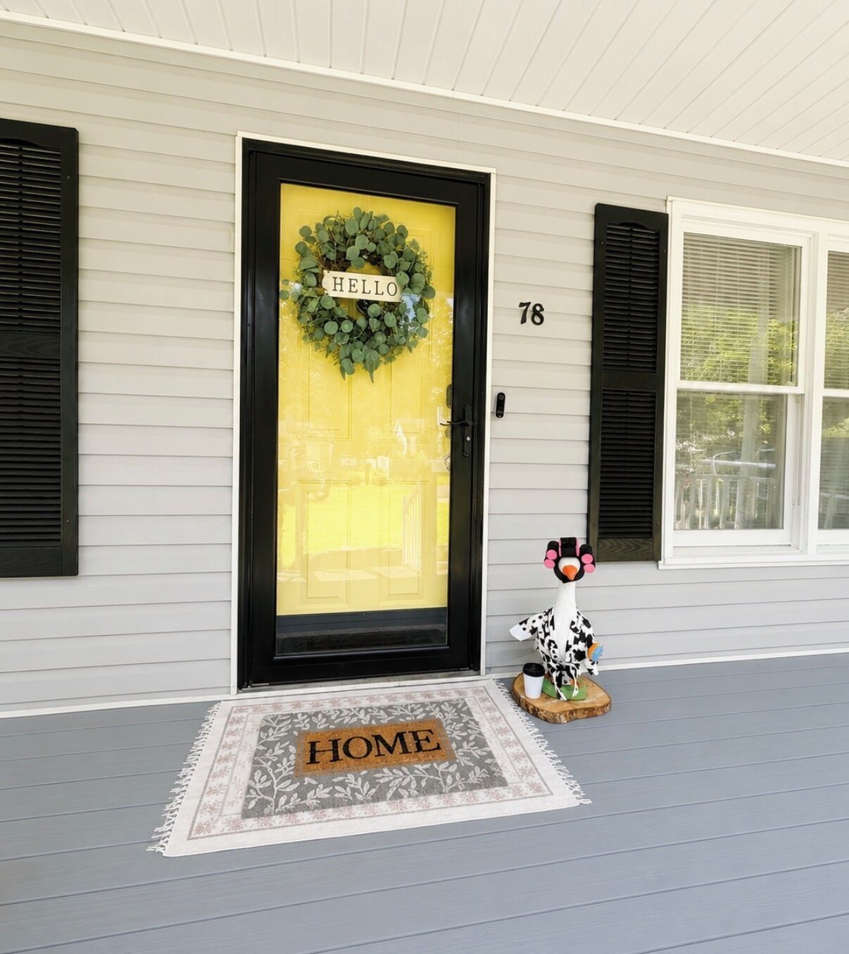 A house with a yellow door, a 'HELLO' wreath, and a 'HOME' mat on the porch.