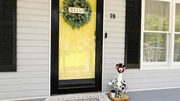 Une maison avec une porte jaune, une couronne décorative sur laquelle est écrit « BONJOUR » et un paillasson avec le mot « MAISON » devant le porche.